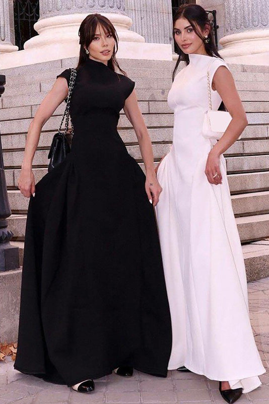 A woman models a formal white sleeveless maxi dress featuring a high neckline, fitted bodice, and dramatic voluminous skirt with structured hip gathering, standing on brick steps.