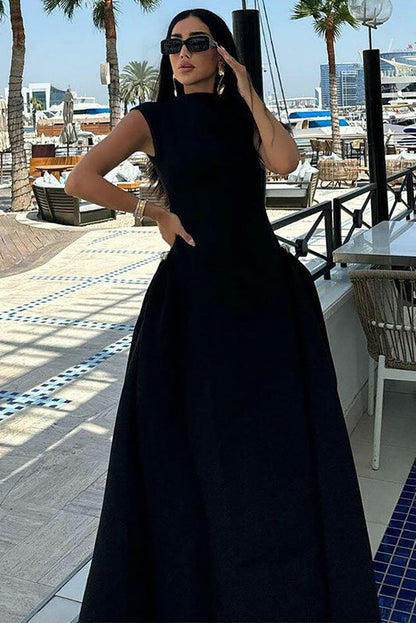 A woman models a formal white sleeveless maxi dress featuring a high neckline, fitted bodice, and dramatic voluminous skirt with structured hip gathering, standing on brick steps.