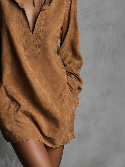 Brown - A model wears a tan suede-textured mini dress featuring a high stand collar, a deep V-neckline with embroidered border detailing, long sleeves, and side pockets against a textured grey background.