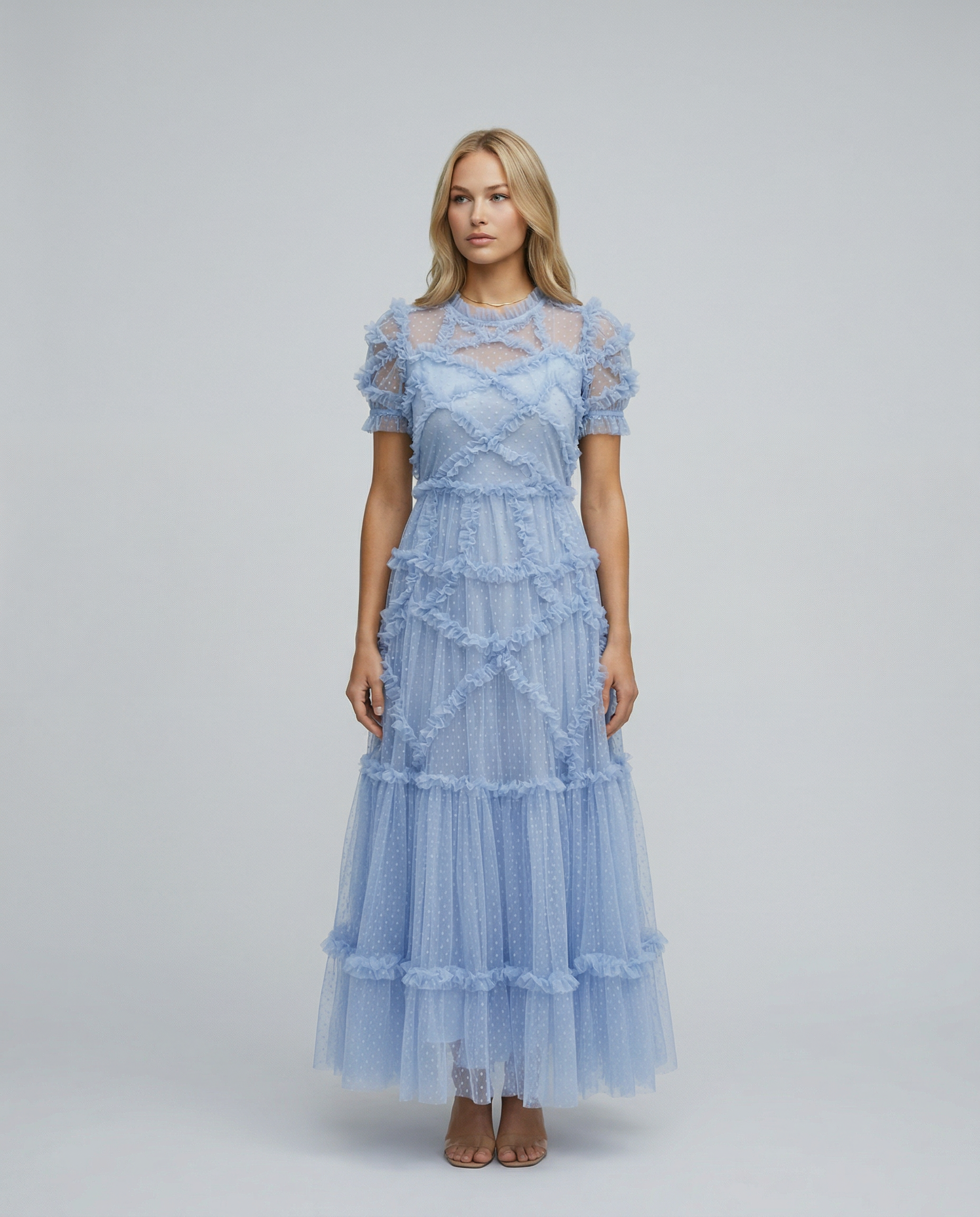 Blue - A woman wearing a light blue Swiss dot tulle maxi dress with a high neck, tiered skirt, and ruffled chevron detailing.