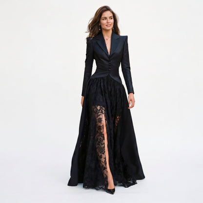 Black - A model poses in a structured black hybrid gown featuring a long-sleeve blazer-style bodice with peak lapels and a button-front closure, paired with a flowing floor-length skirt showcasing a sheer floral lace underlay and a high leg slit.