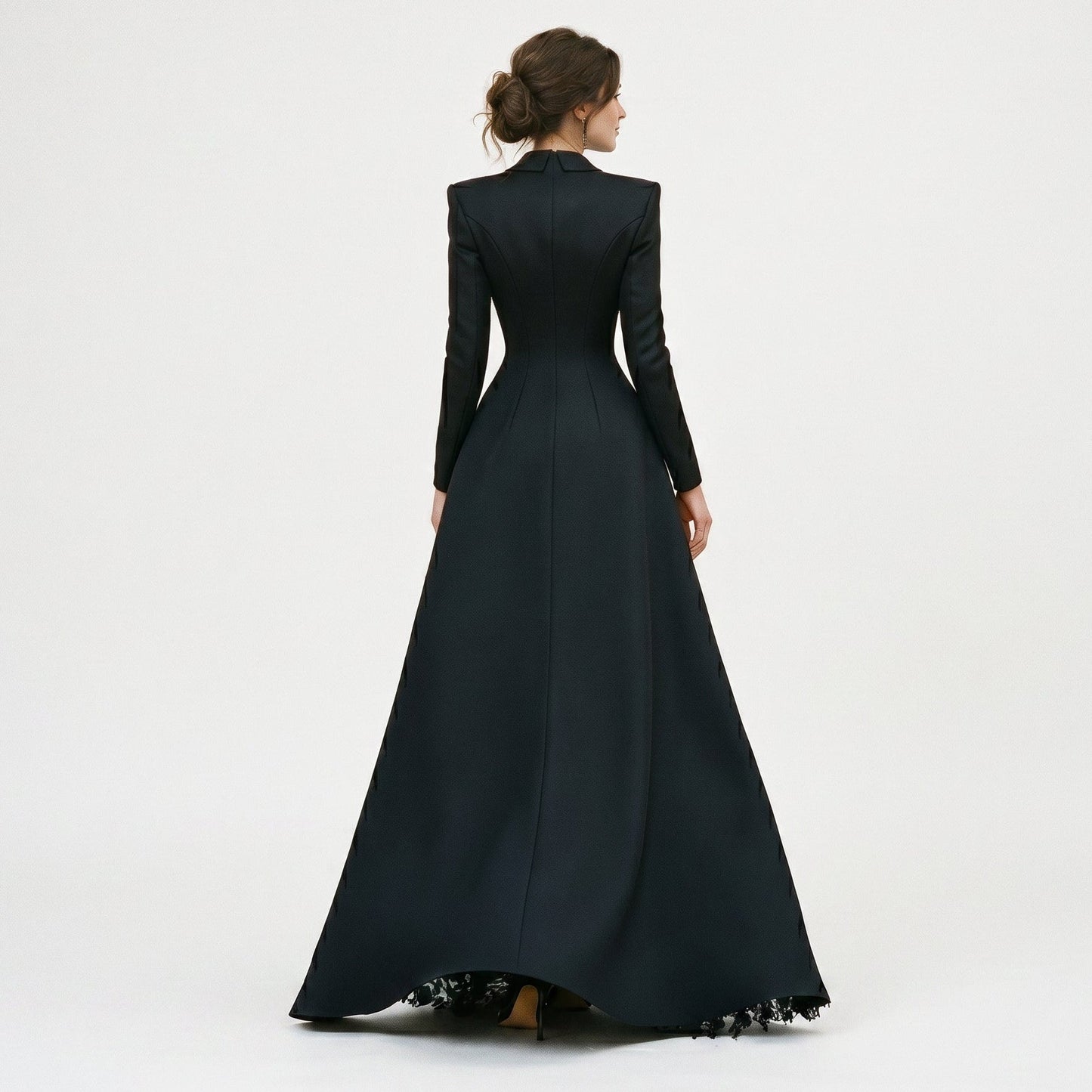 Black - A model poses in a structured black hybrid gown featuring a long-sleeve blazer-style bodice with peak lapels and a button-front closure, paired with a flowing floor-length skirt showcasing a sheer floral lace underlay and a high leg slit.