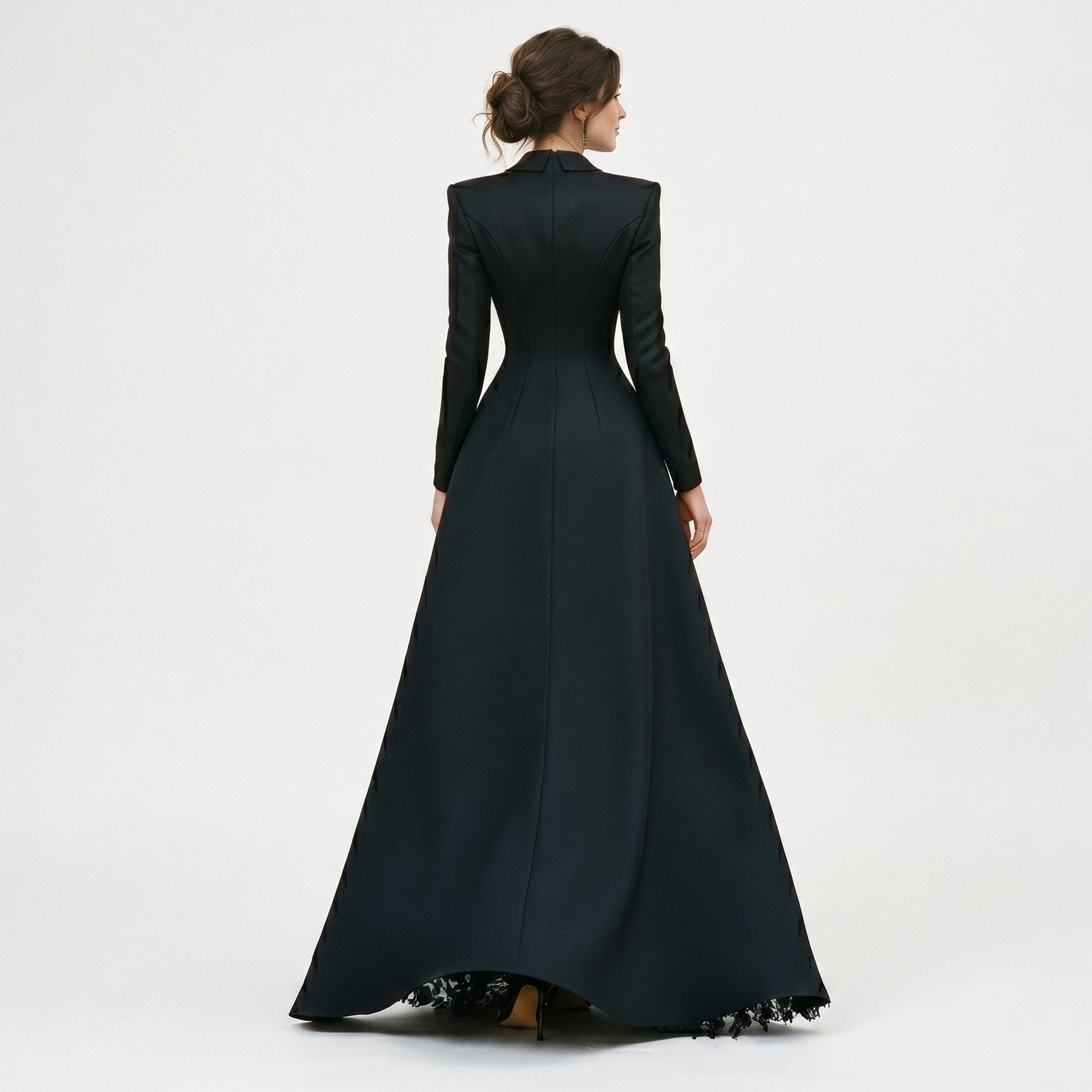 Black - A model poses in a structured black hybrid gown featuring a long-sleeve blazer-style bodice with peak lapels and a button-front closure, paired with a flowing floor-length skirt showcasing a sheer floral lace underlay and a high leg slit.