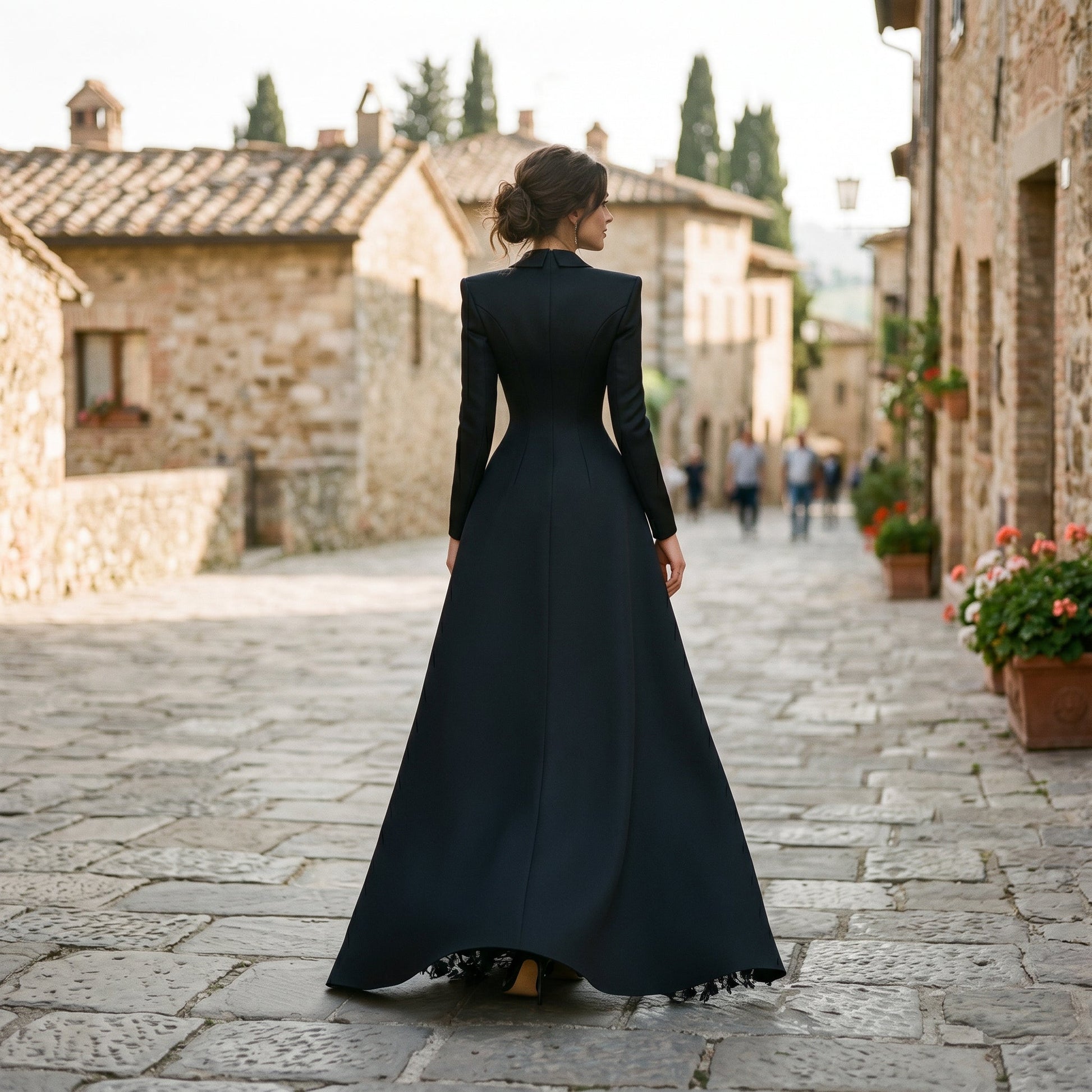 Black - A model poses in a structured black hybrid gown featuring a long-sleeve blazer-style bodice with peak lapels and a button-front closure, paired with a flowing floor-length skirt showcasing a sheer floral lace underlay and a high leg slit.