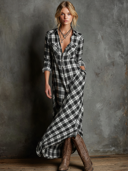 Black - A woman wearing a green and brown tartan plaid maxi shirt dress with a button-down front, long sleeves rolled up, and chest pockets, paired with brown leather cowboy boots against a textured grey wall.