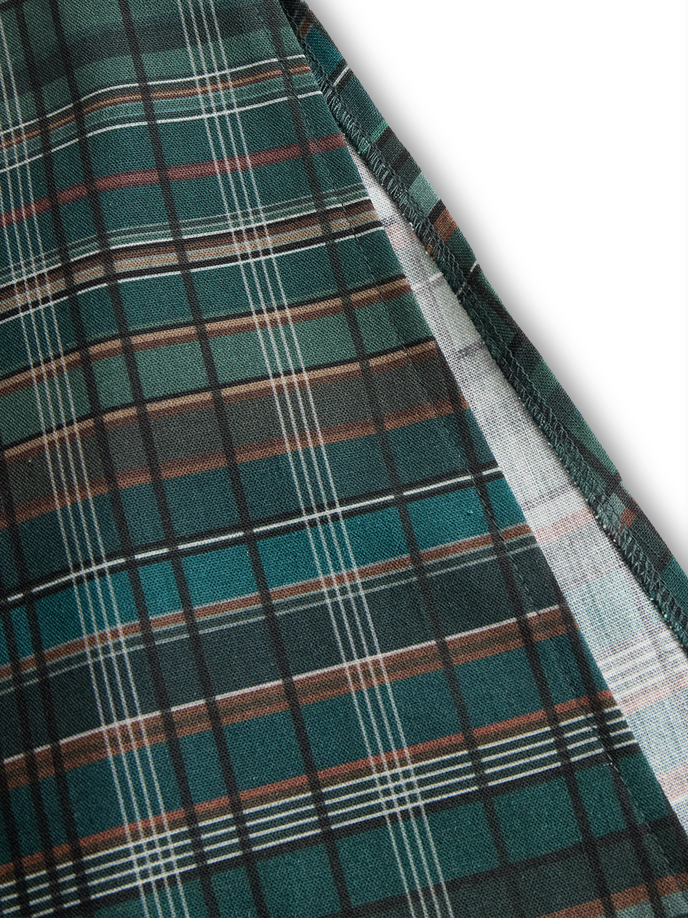 Black - A woman wearing a green and brown tartan plaid maxi shirt dress with a button-down front, long sleeves rolled up, and chest pockets, paired with brown leather cowboy boots against a textured grey wall.