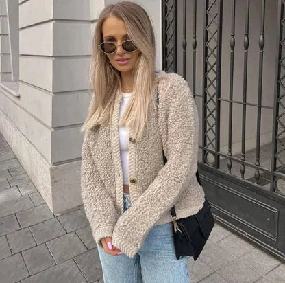 A woman wearing a beige, textured boucle knit cardigan with a button-front closure, ribbed trims, and gold-tone buttons, styled casually over a white top and light blue jeans.