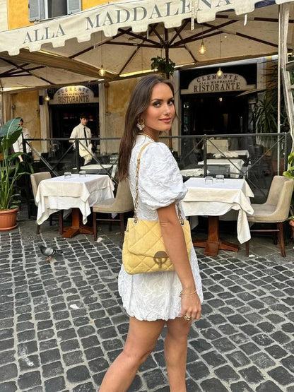 White - Women's white mini dress featuring a deep V-neckline, short puff sleeves, a structured bubble hem, and an all-over raised textured pattern, worn outdoors.