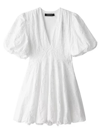 White - Women's white mini dress featuring a deep V-neckline, short puff sleeves, a structured bubble hem, and an all-over raised textured pattern, worn outdoors.