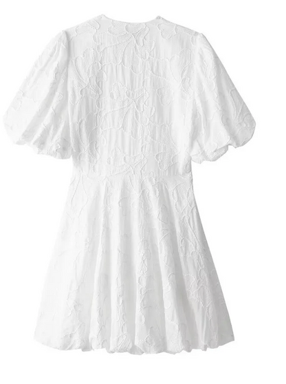 White - Women's white mini dress featuring a deep V-neckline, short puff sleeves, a structured bubble hem, and an all-over raised textured pattern, worn outdoors.