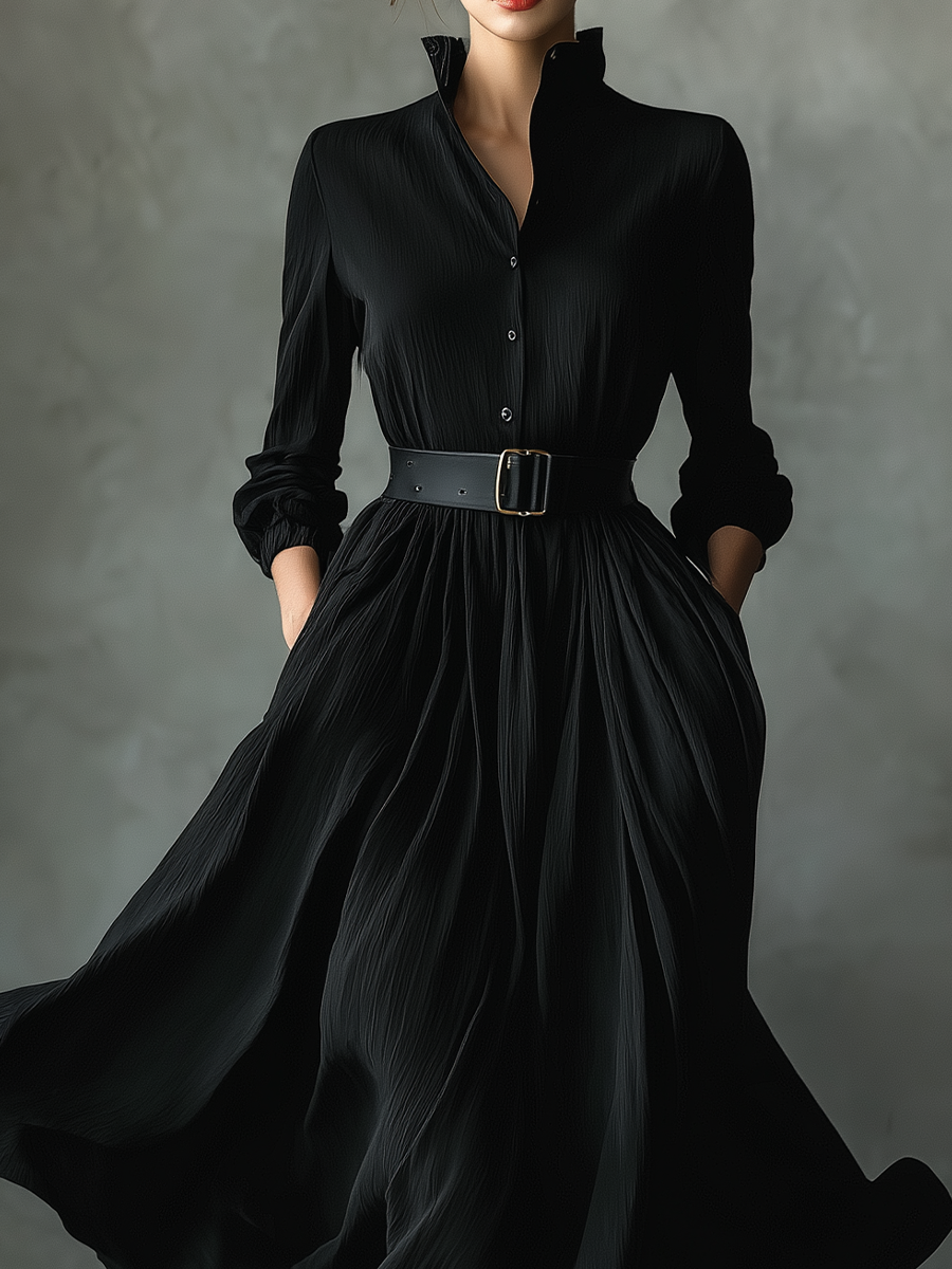 Black - A woman wearing a long-sleeved black textured crepe maxi dress with a high stand collar, button-up front, and a wide black belt with a gold buckle, showing a voluminous flowing skirt with hands in pockets.