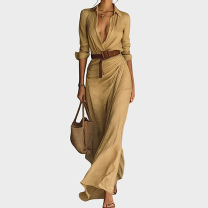 A woman wearing a sand-coloured, textured crepe maxi shirt dress with a plunging collared neckline, ruched waist detailing, and a draped wrap-effect skirt.