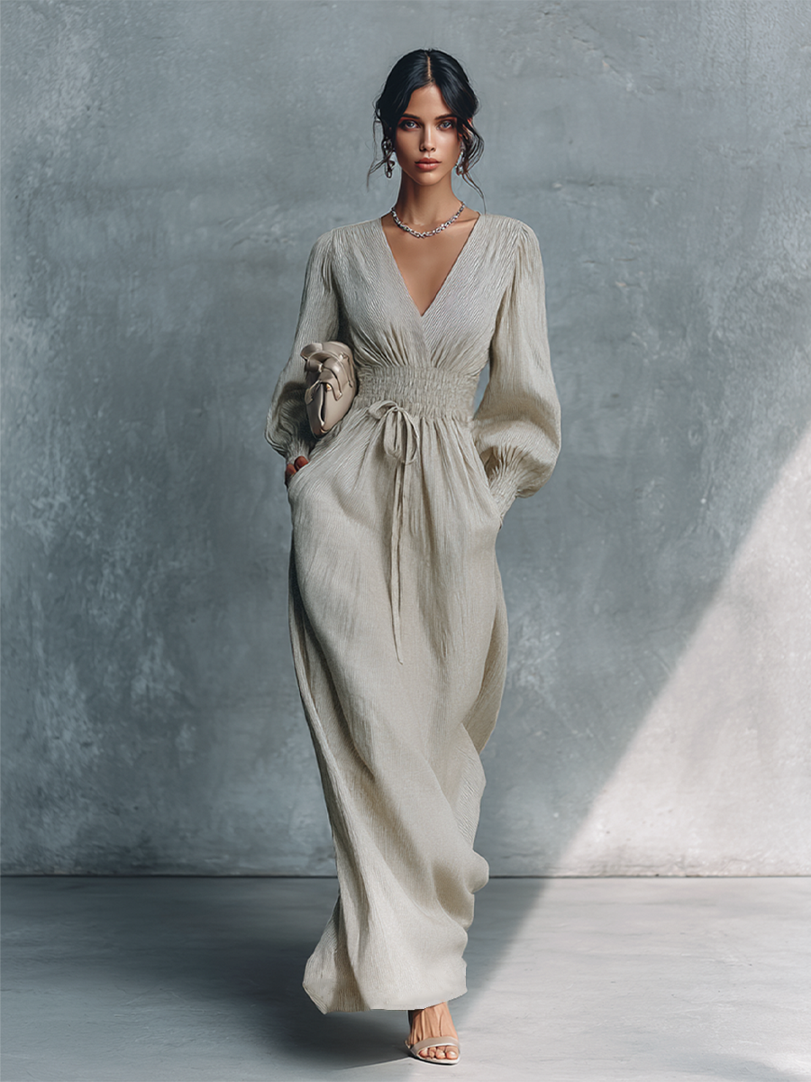 Beige - A woman wearing a champagne-coloured, crinkle-textured crepe maxi dress featuring a plunging V-neckline, long balloon sleeves with shirred cuffs, a smocked waistband with a drawstring, and a flowing floor-length skirt.