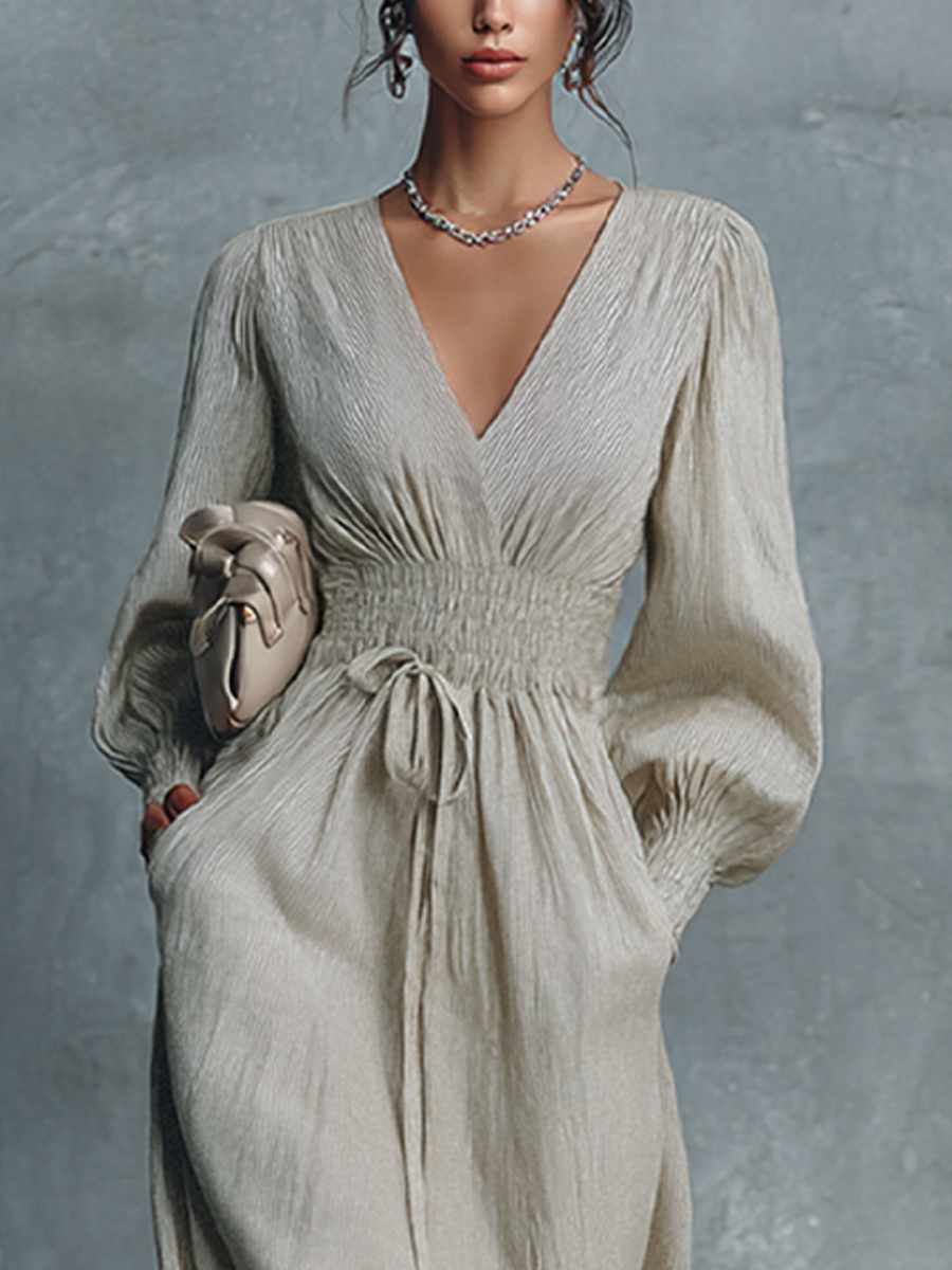 Beige - A woman wearing a champagne-coloured, crinkle-textured crepe maxi dress featuring a plunging V-neckline, long balloon sleeves with shirred cuffs, a smocked waistband with a drawstring, and a flowing floor-length skirt.