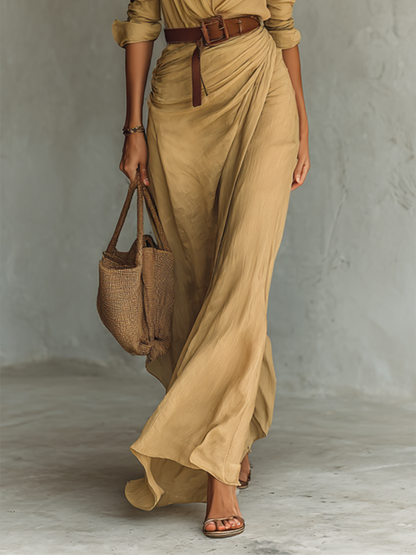 Khaki - A woman wearing a sand-coloured textured crepe maxi shirt dress with a collared neckline, unbuttoned front, ruched draped waist, and long sleeves, accessorised with a brown leather belt.