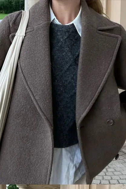Grey - A woman walking outdoors wearing a taupe-coloured, textured double-breasted short pea coat with wide notched lapels and an oversized fit, styled over a black top and high boots.