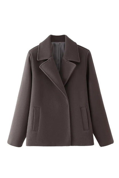Grey - A woman walking outdoors wearing a taupe-coloured, textured double-breasted short pea coat with wide notched lapels and an oversized fit, styled over a black top and high boots.