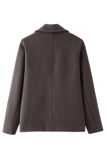 Grey - A woman walking outdoors wearing a taupe-coloured, textured double-breasted short pea coat with wide notched lapels and an oversized fit, styled over a black top and high boots.