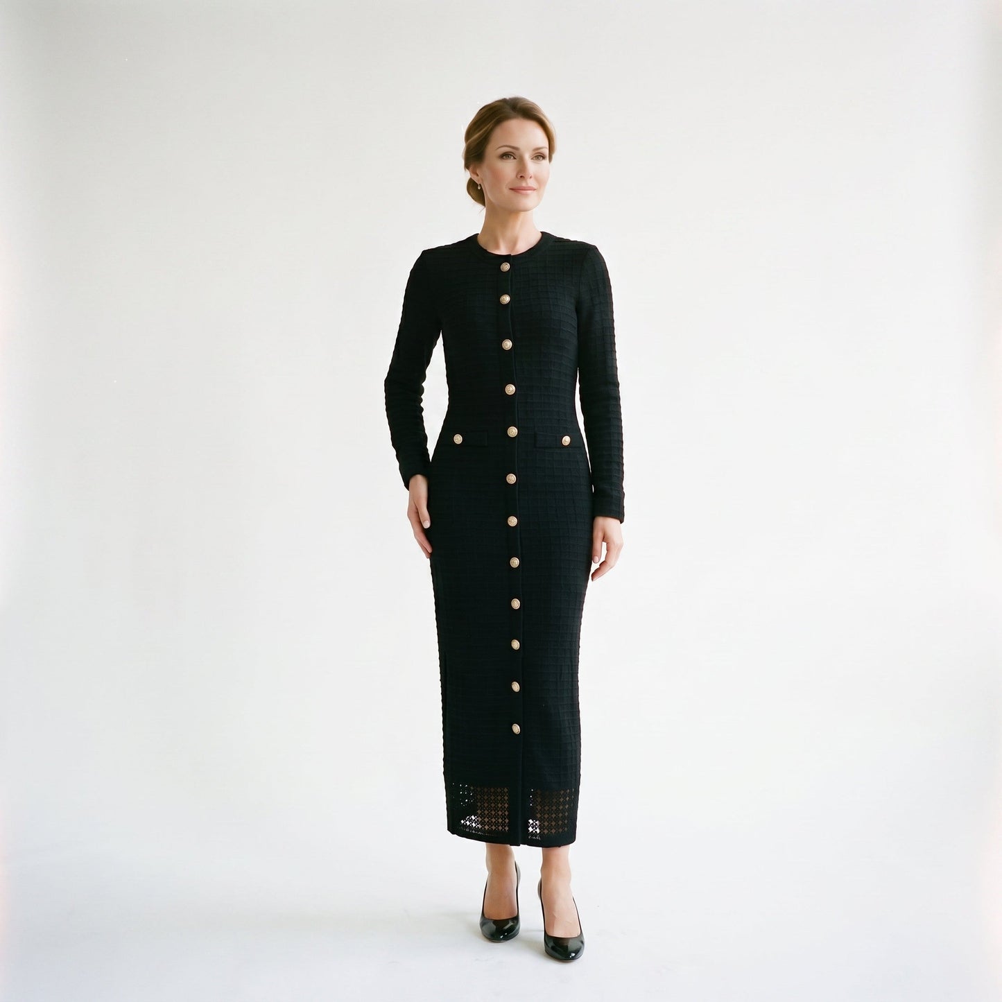 Black - A woman wearing a long-sleeve black textured knit column midi dress featuring gold-tone buttons down the front and a pointelle hem, set against a plain white background.