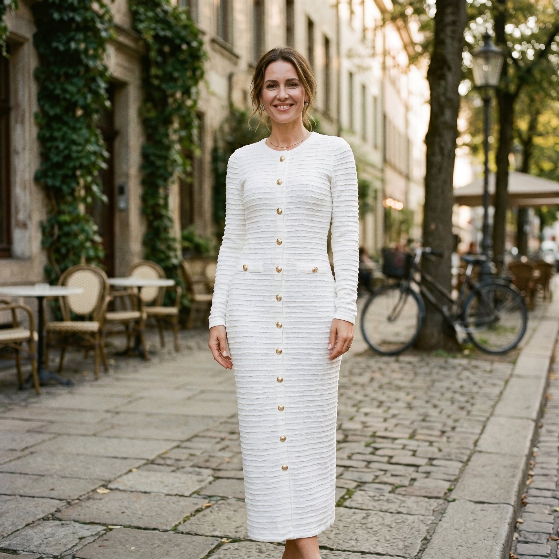 Black - A woman wearing a long-sleeve black textured knit column midi dress featuring gold-tone buttons down the front and a pointelle hem, set against a plain white background.