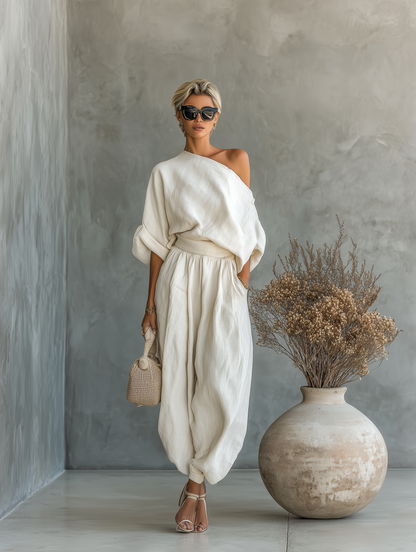 Off-white - A woman wearing an elegant cream-coloured, textured linen one-shoulder jumpsuit with a draped balloon sleeve, structured waistband, and voluminous tapered trousers.