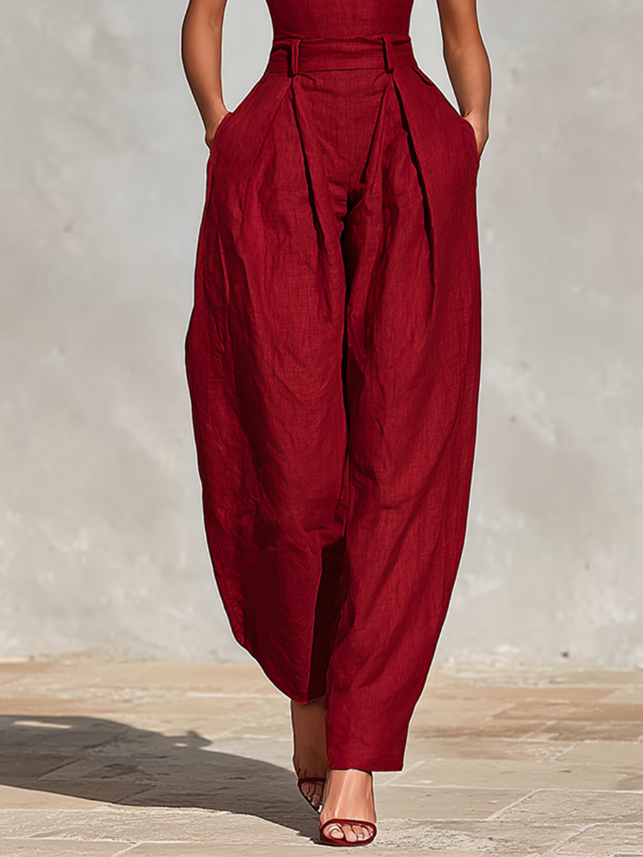 Red - A model wearing a deep red, textured linen wide-leg jumpsuit featuring a plunging V-neckline, structured high waist, and pleated trousers.