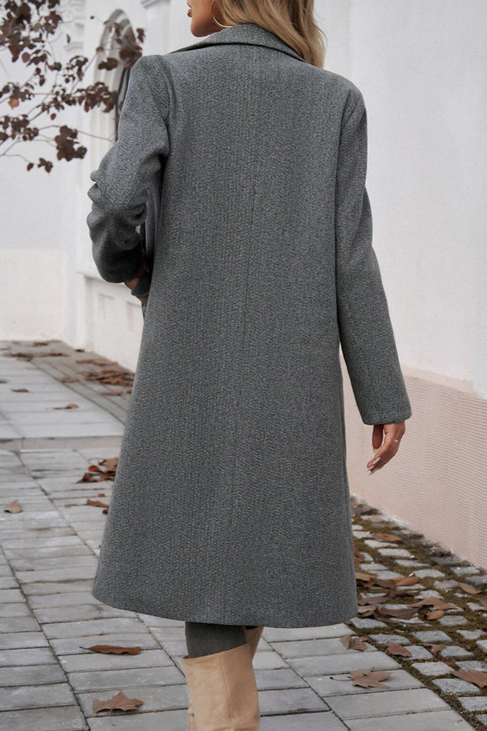 Gray - A woman wearing a grey textured mid-length coat with notch lapels and flap pockets, styled over a white V-neck t-shirt and distressed grey jeans.