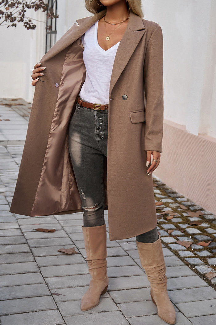 Brown - A woman wearing a grey textured mid-length coat with notch lapels and flap pockets, styled over a white V-neck t-shirt and distressed grey jeans.
