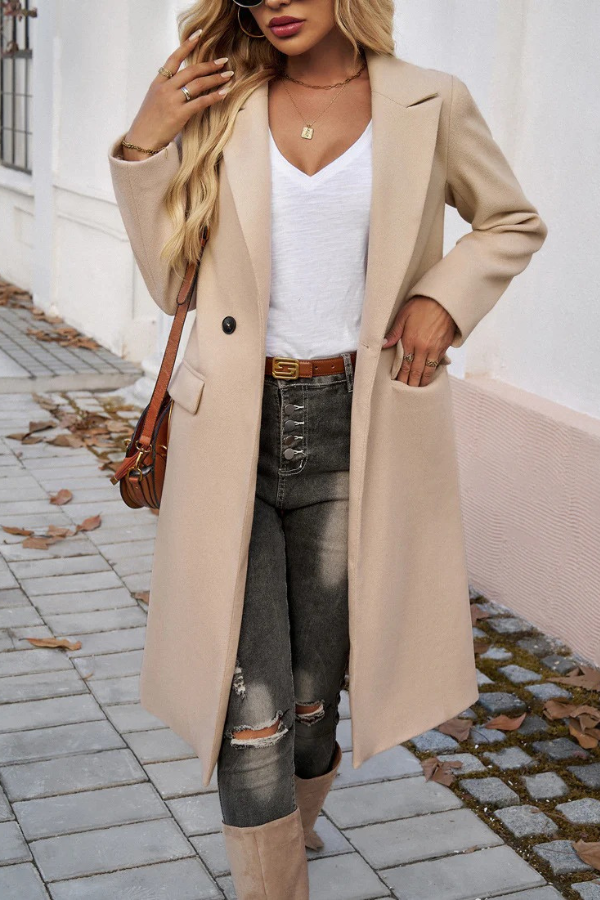 Beige - A woman wearing a grey textured mid-length coat with notch lapels and flap pockets, styled over a white V-neck t-shirt and distressed grey jeans.