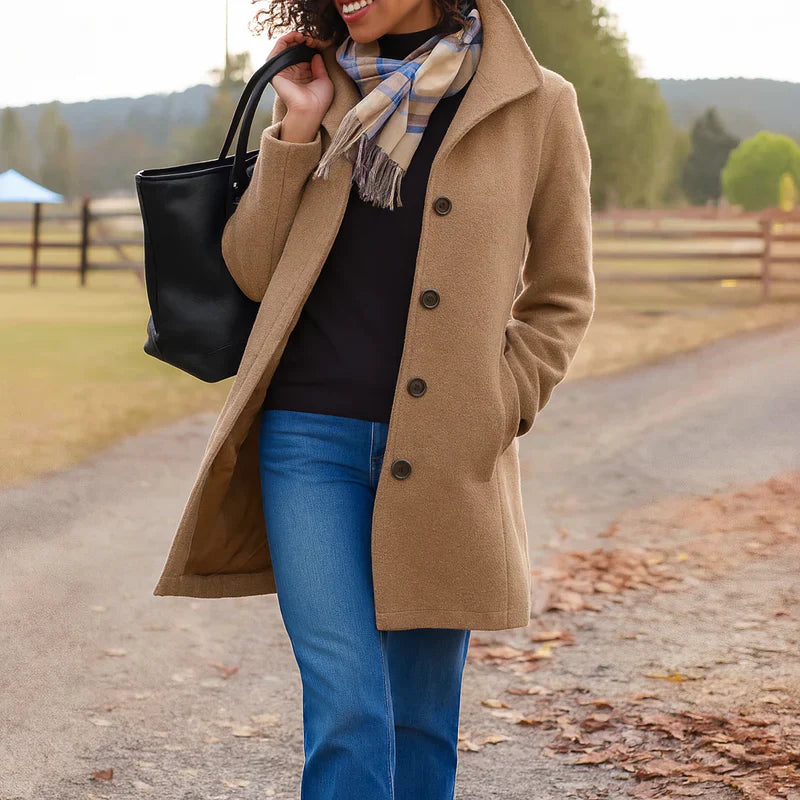 Brown - A woman walking outdoors wearing a camel-coloured, mid-length textured coat with a stand collar and single-breasted button closure, styled with blue jeans and a scarf.