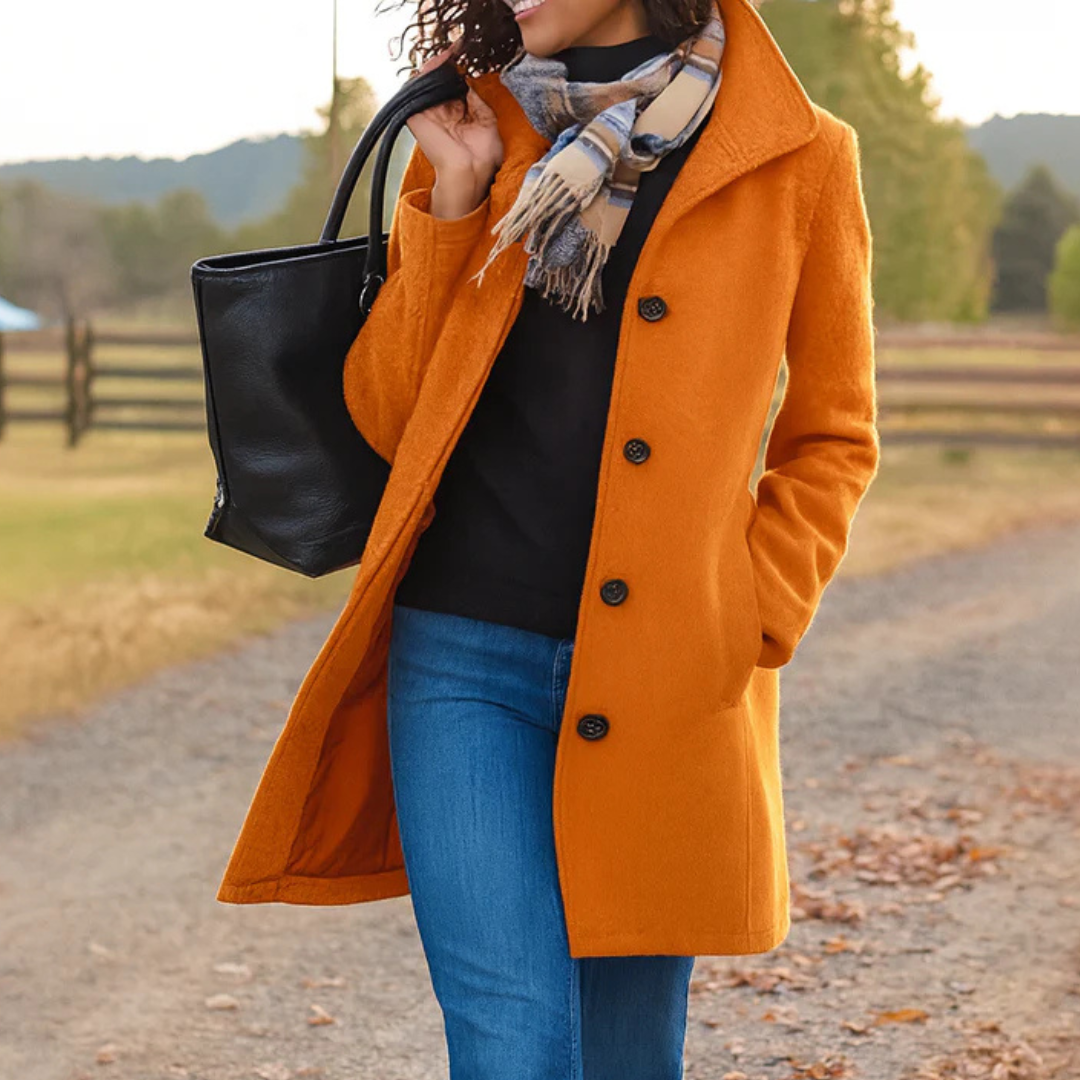 Orange - A woman walking outdoors wearing a camel-coloured, mid-length textured coat with a stand collar and single-breasted button closure, styled with blue jeans and a scarf.