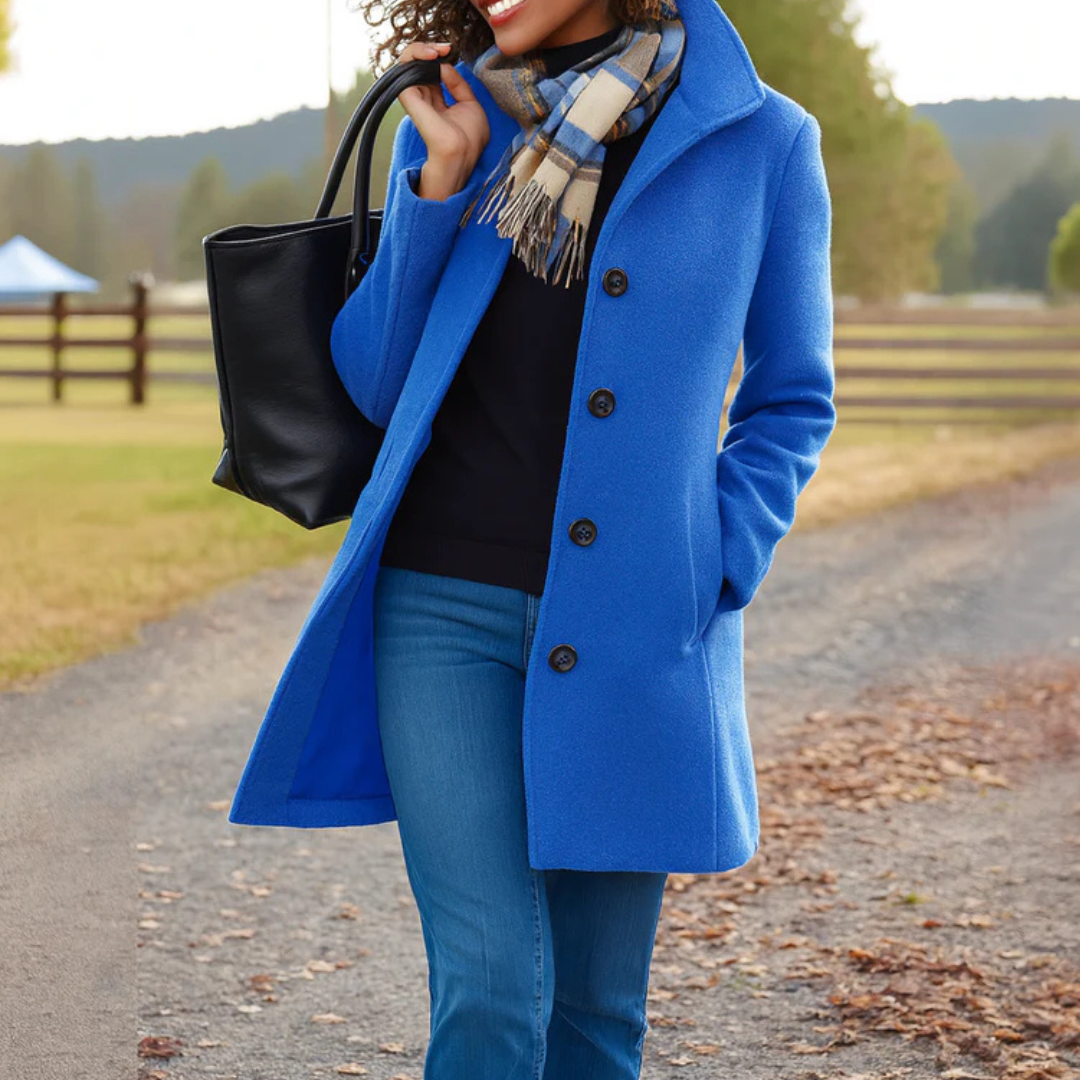 Blue - A woman walking outdoors wearing a camel-coloured, mid-length textured coat with a stand collar and single-breasted button closure, styled with blue jeans and a scarf.