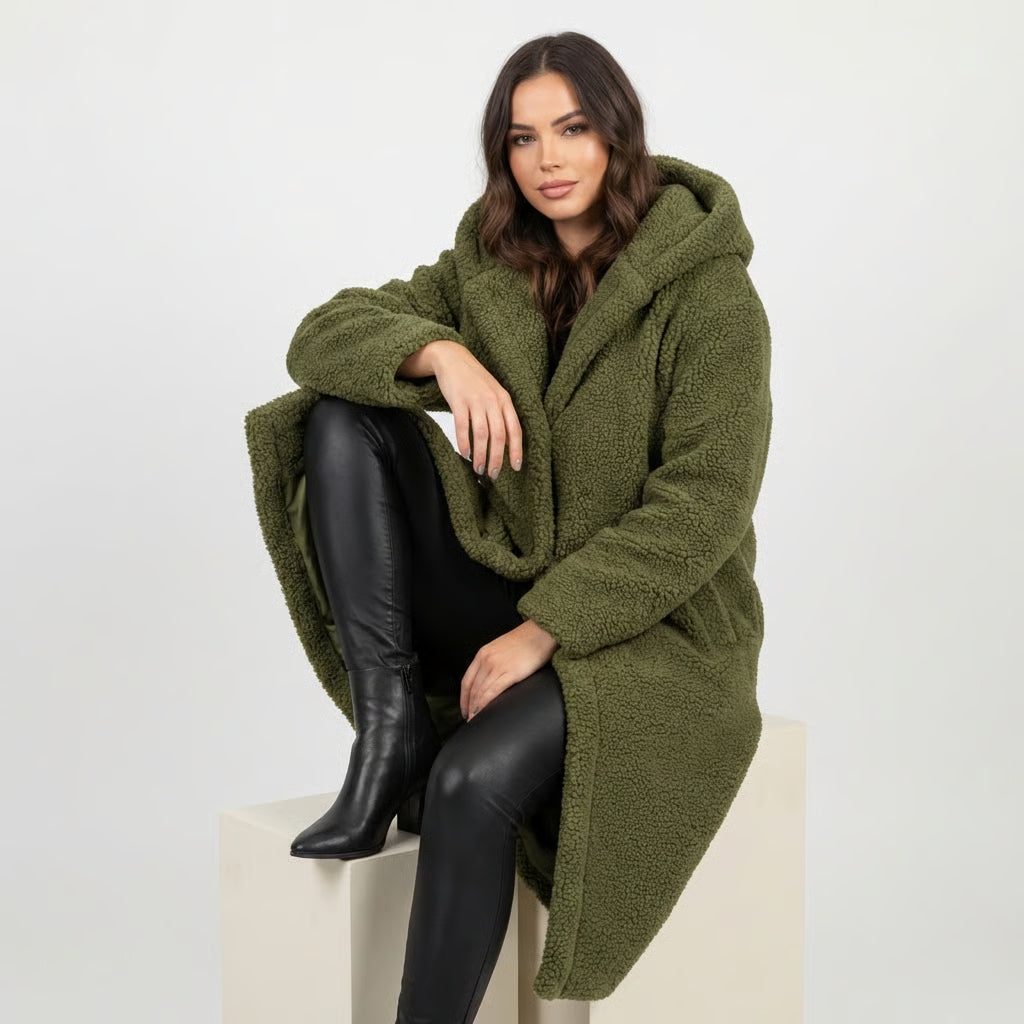 Green - A woman wearing a mid-length olive green textured teddy coat with a large hood, styled over a black turtleneck sweater and black sunglasses against a plain white background.