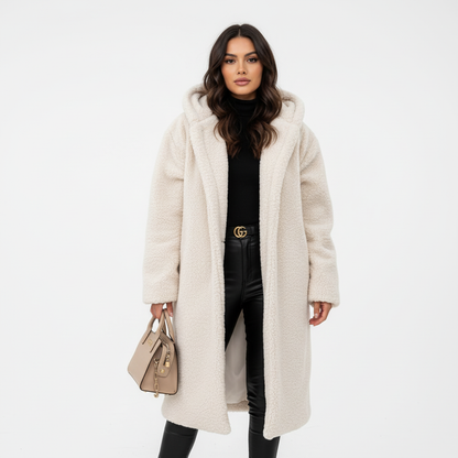 White - A woman wearing a mid-length olive green textured teddy coat with a large hood, styled over a black turtleneck sweater and black sunglasses against a plain white background.