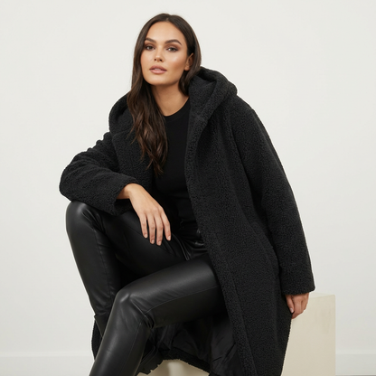 Black - A woman wearing a mid-length olive green textured teddy coat with a large hood, styled over a black turtleneck sweater and black sunglasses against a plain white background.