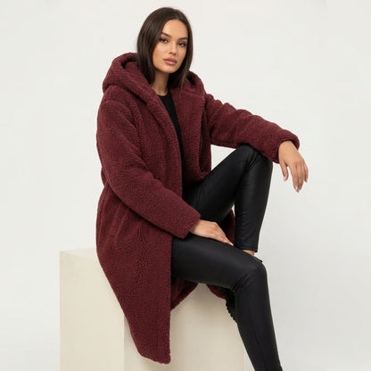 Red - A woman wearing a mid-length olive green textured teddy coat with a large hood, styled over a black turtleneck sweater and black sunglasses against a plain white background.