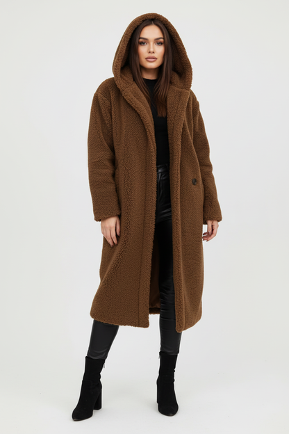 Brown - A woman wearing a mid-length olive green textured teddy coat with a large hood, styled over a black turtleneck sweater and black sunglasses against a plain white background.