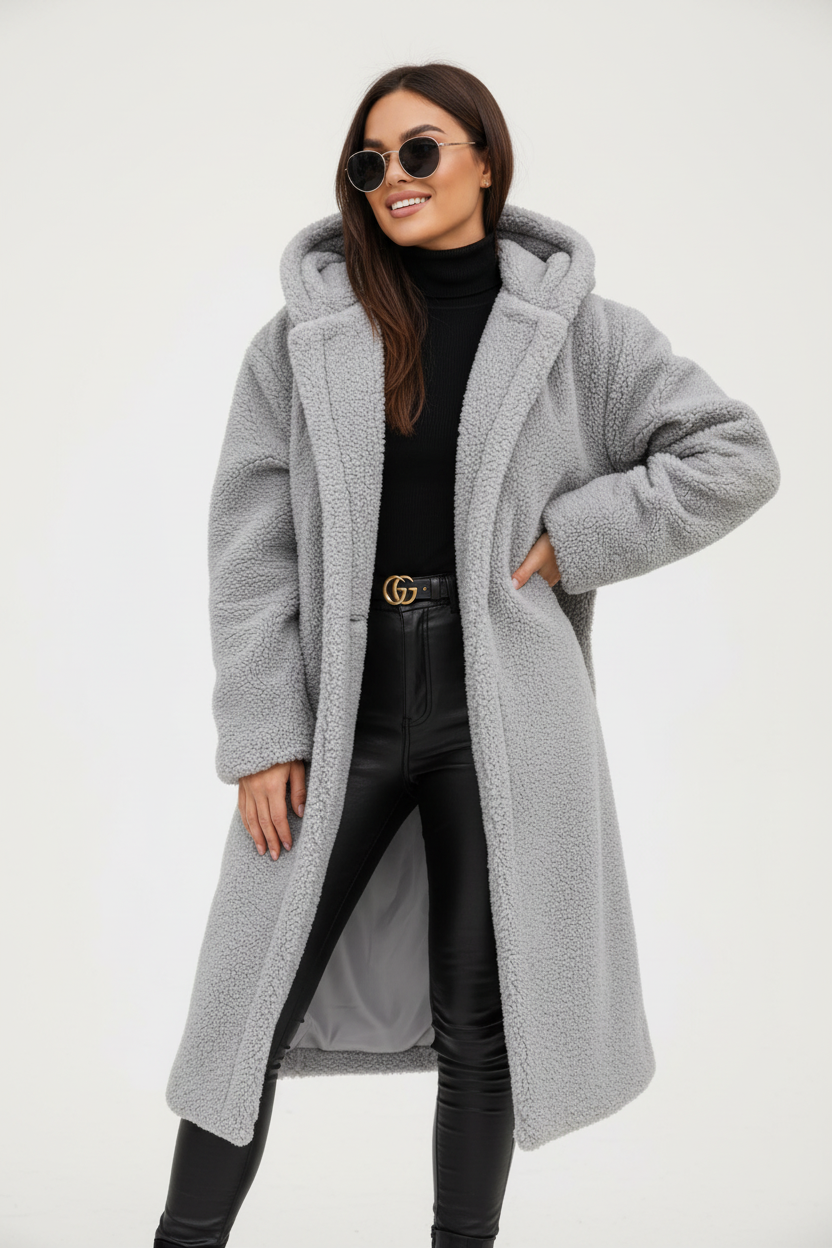 Grey - A woman wearing a mid-length olive green textured teddy coat with a large hood, styled over a black turtleneck sweater and black sunglasses against a plain white background.