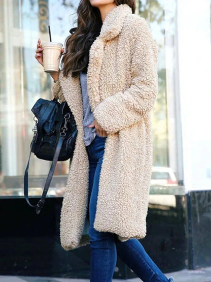 Beige - A woman wearing a cream-coloured, longline textured teddy coat with oversized lapels, styled over a grey t-shirt and blue jeans.