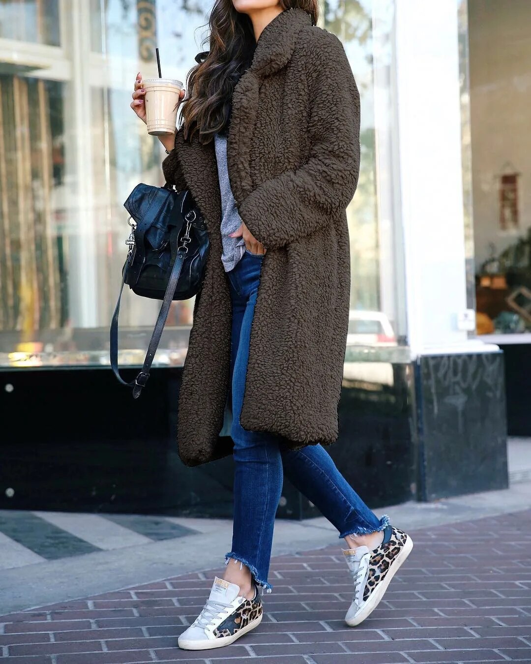 Dark gray - A woman walking on a city street wearing a knee-length, beige textured teddy coat with notch lapels, styled over a grey top and blue denim jeans.