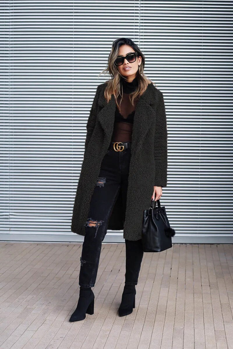 Black - A woman walking on a city street wearing a knee-length, beige textured teddy coat with notch lapels, styled over a grey top and blue denim jeans.