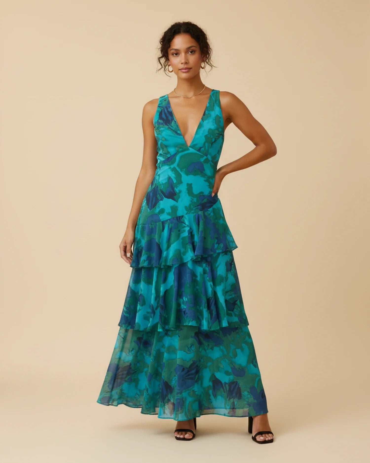Green - A woman models a formal plunging V-neck maxi dress featuring a vibrant teal and navy abstract print and a flowing tiered skirt.