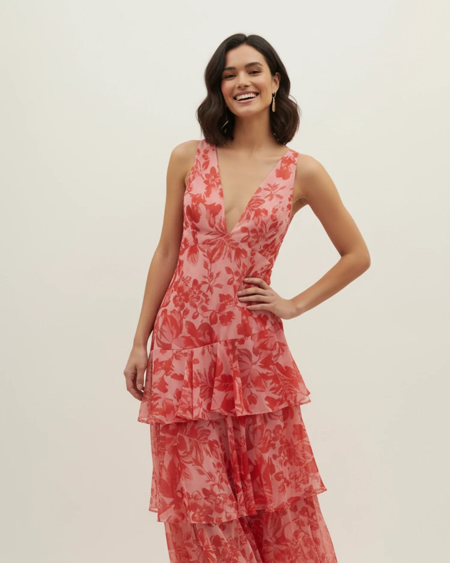 Red - A woman models a formal plunging V-neck maxi dress featuring a vibrant teal and navy abstract print and a flowing tiered skirt.