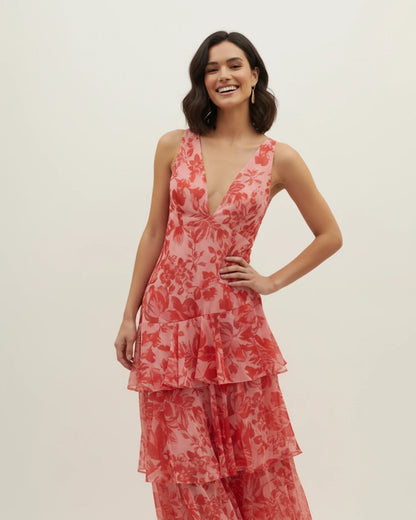 Red - A woman models a formal plunging V-neck maxi dress featuring a vibrant teal and navy abstract print and a flowing tiered skirt.
