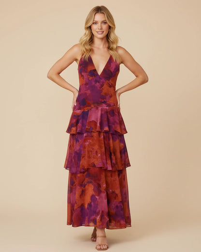 Purple - A woman models a formal plunging V-neck maxi dress featuring a vibrant teal and navy abstract print and a flowing tiered skirt.