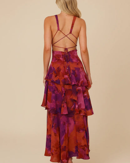 Purple - A woman models a formal plunging V-neck maxi dress featuring a vibrant teal and navy abstract print and a flowing tiered skirt.