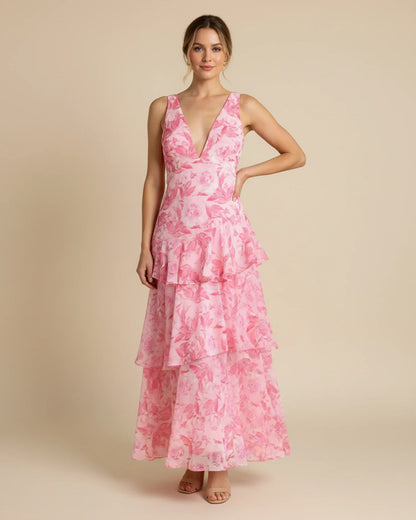 Pink - A woman models a formal plunging V-neck maxi dress featuring a vibrant teal and navy abstract print and a flowing tiered skirt.