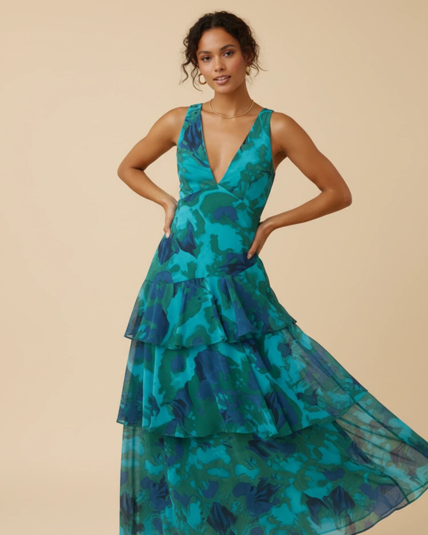 Green - A woman models a formal plunging V-neck maxi dress featuring a vibrant teal and navy abstract print and a flowing tiered skirt.