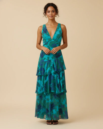Green - A woman models a formal plunging V-neck maxi dress featuring a vibrant teal and navy abstract print and a flowing tiered skirt.