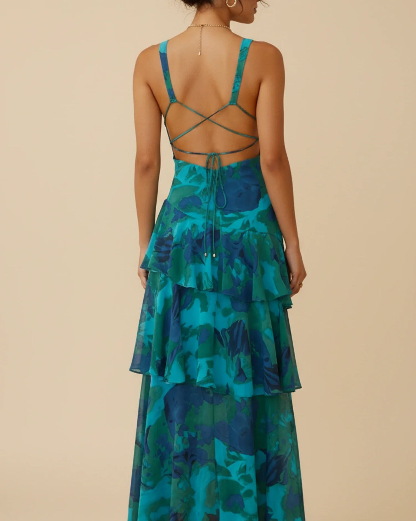 Green - A woman models a formal plunging V-neck maxi dress featuring a vibrant teal and navy abstract print and a flowing tiered skirt.